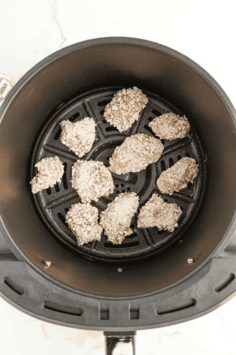 Dredged chicken pieces arranged in an oiled air fryer basket, lightly sprayed with cooking oil, ready to cook at 380&deg;F, being shaken halfway through for even crisping.