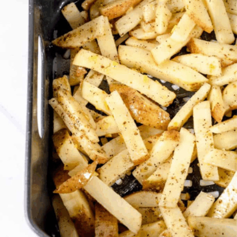 Potatoes arranged in a single layer in the air fryer basket, cooking until golden and crispy, flipped halfway through.