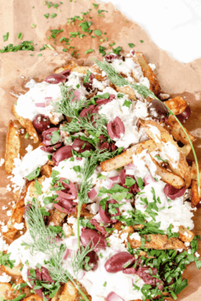 Air Fryer Greek Fries topped with crumbled feta, diced tomatoes, red onions, and Kalamata olives on a white plate.