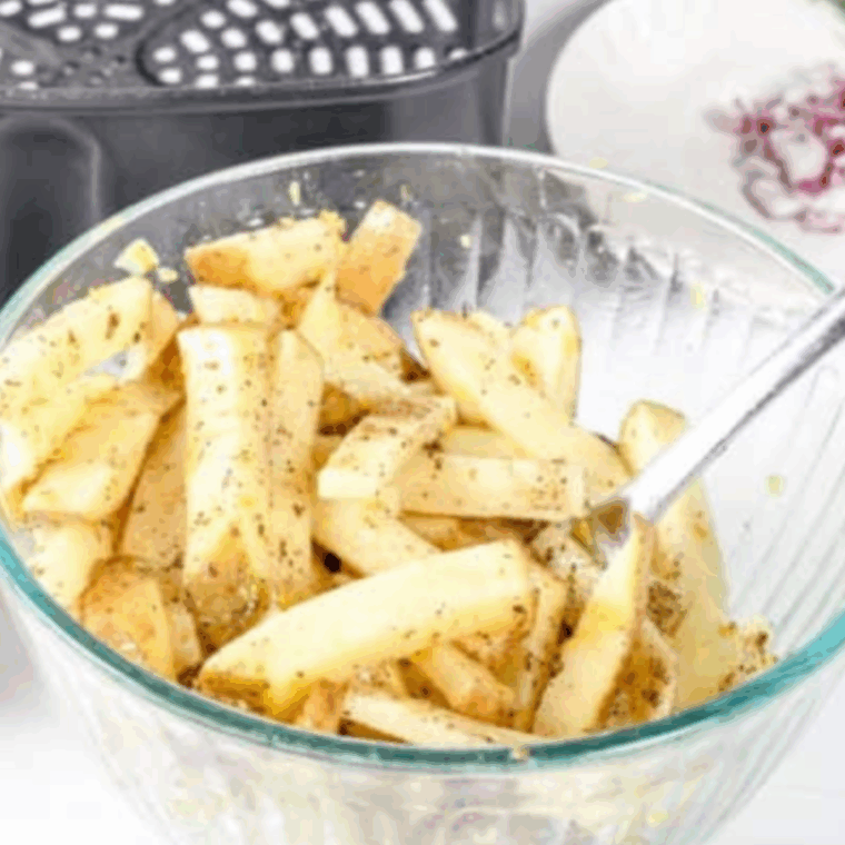 Potatoes sliced into fries, tossed with olive oil, lemon zest, and Greek seasoning in a large bowl.