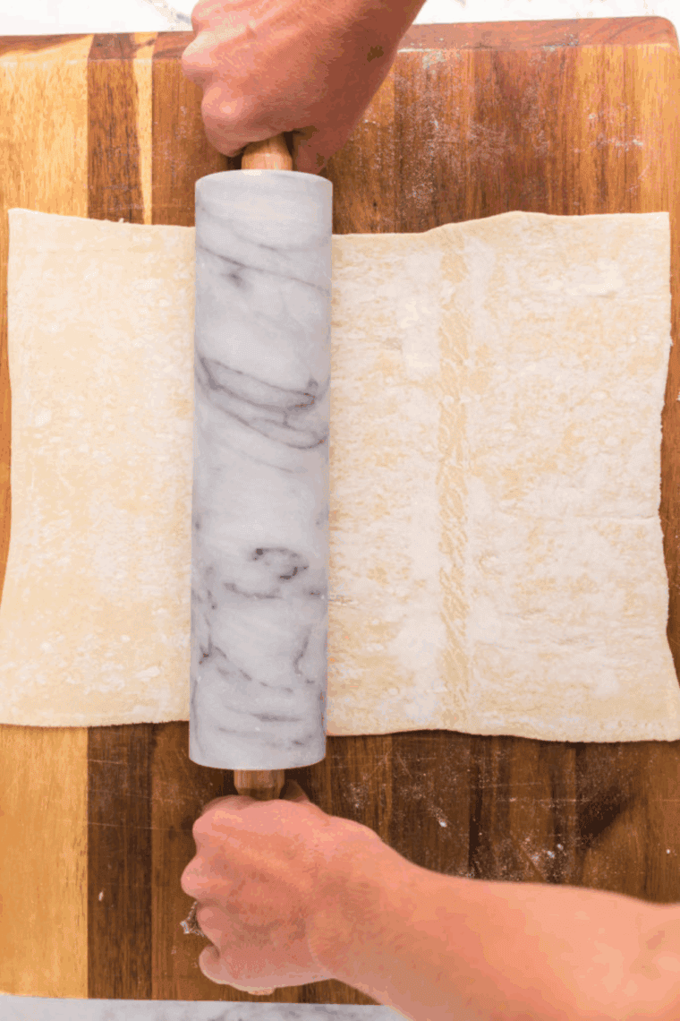 Puff pastry sheet being rolled out on a floured wooden cutting board.