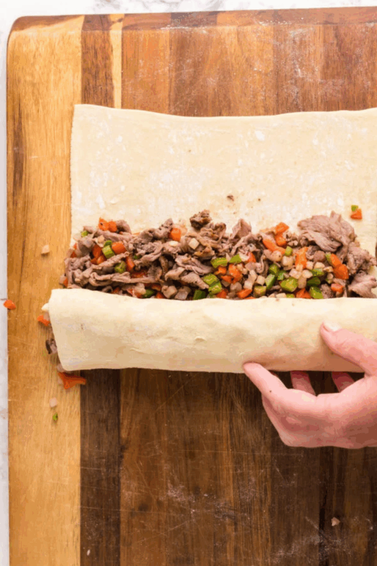 Steak, peppers, and onions spread on puff pastry with provolone cheese, ready to be rolled.