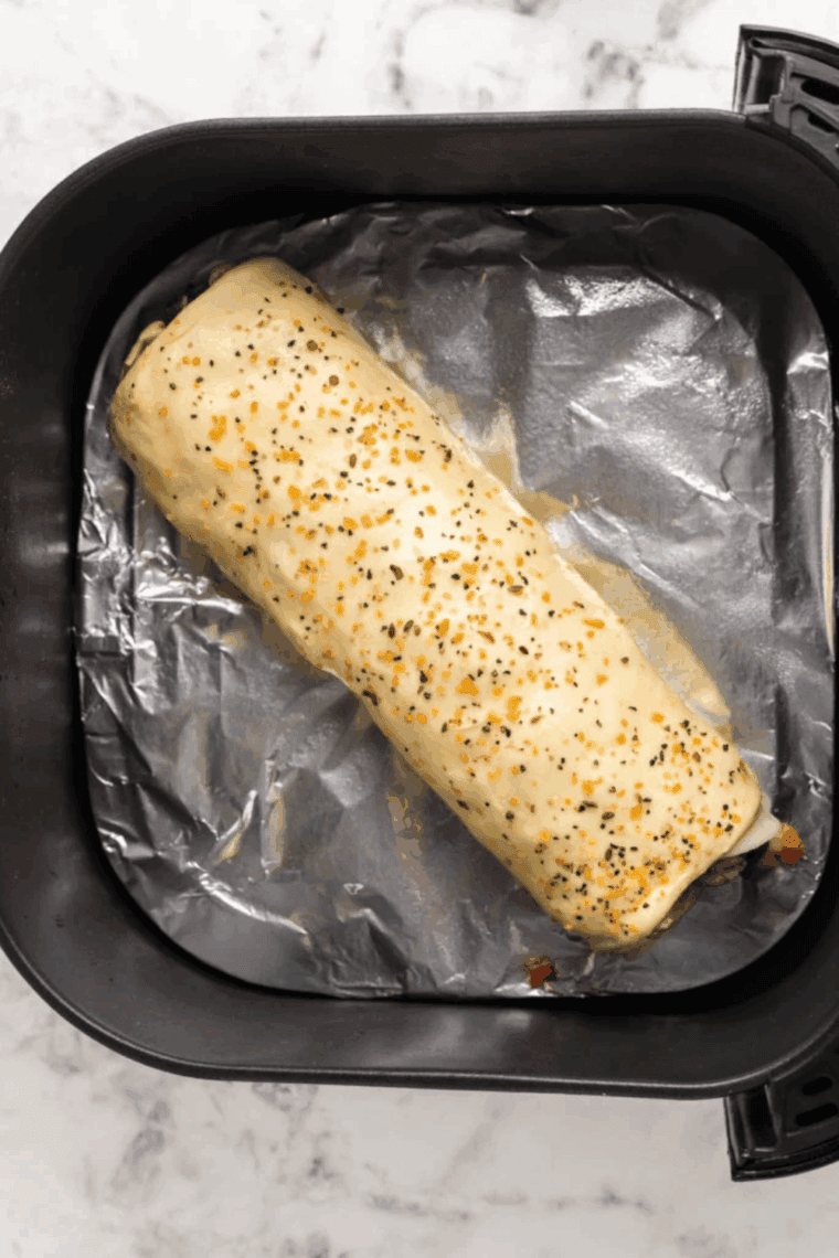 Egg-washed puff pastry sprinkled with Montreal steak seasoning and slits, cooking in the air fryer.