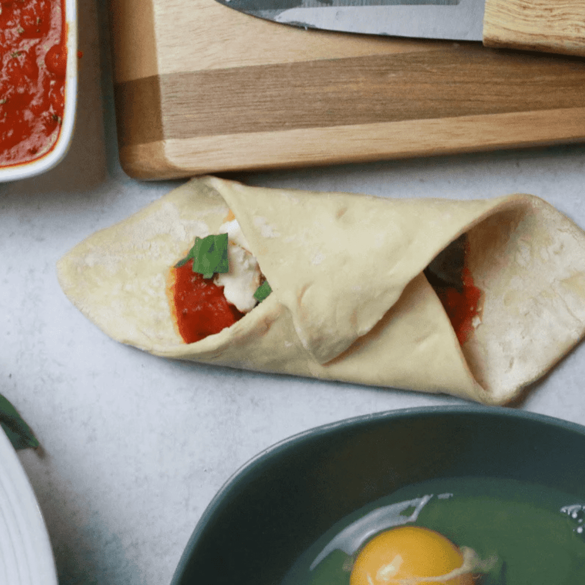 Puff pastry square turned into a diamond shape topped with tomato sauce, mozzarella pieces, and fresh basil leaves.