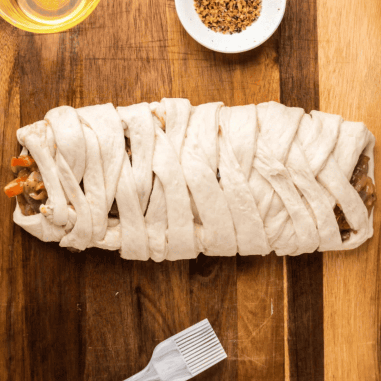 Pizza crust filled with mushrooms and peppers, braided in a crisscross pattern, ready for the air fryer.