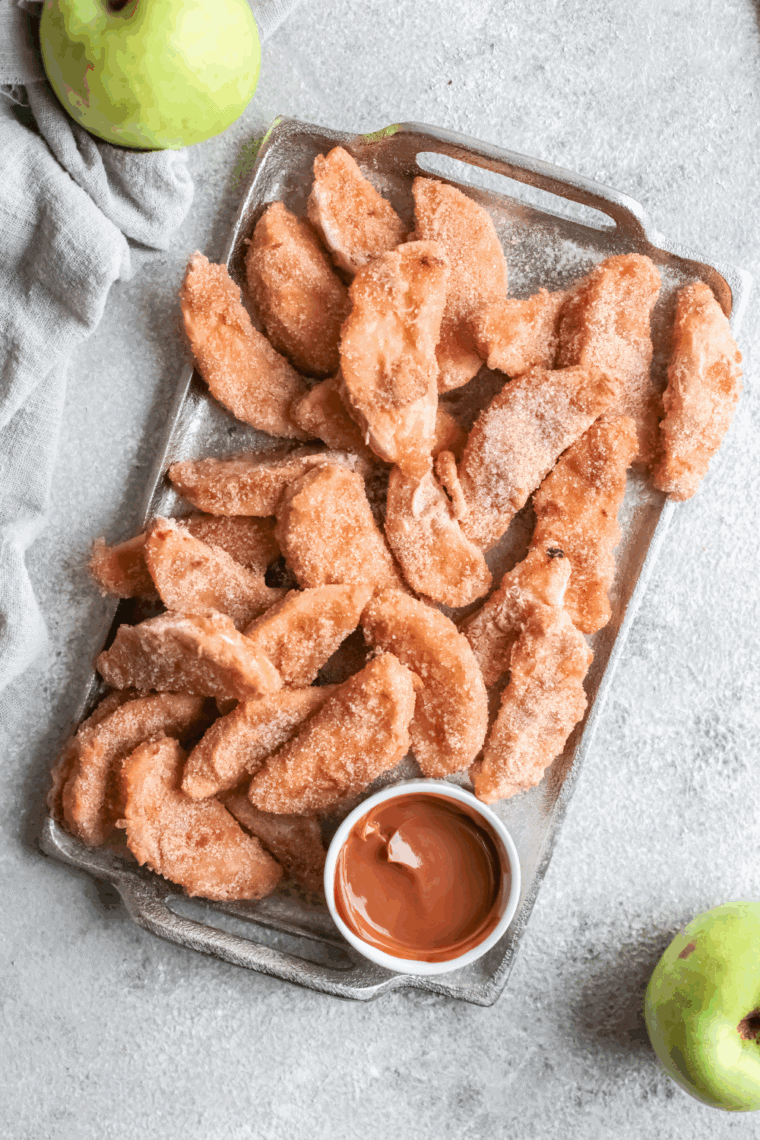 Golden crispy Legoland-style apple fries coated in sweet cinnamon sugar served on a plate with caramel dipping sauce.
