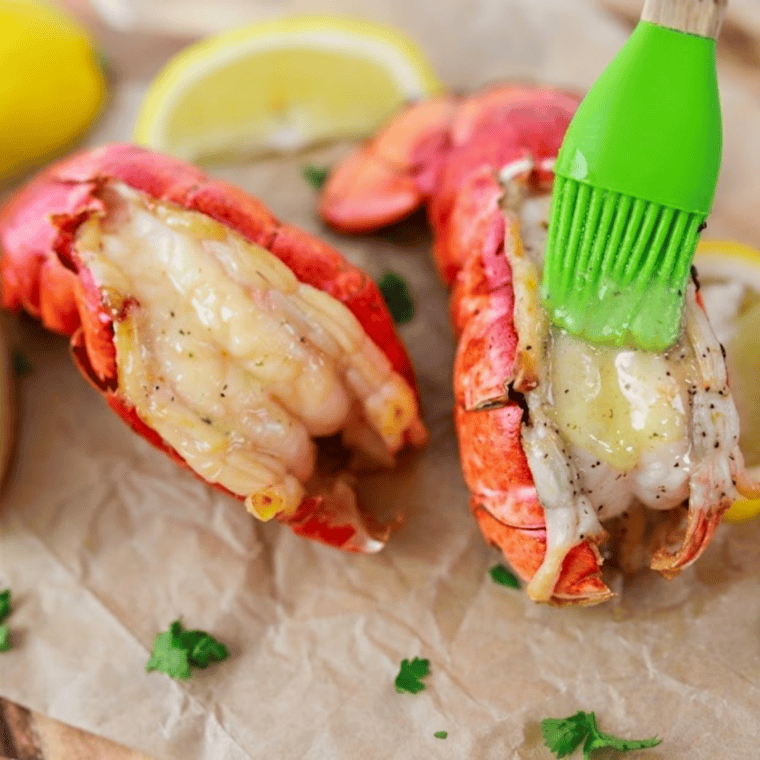 Cooked frozen lobster tails in air fryer basket with lemon wedges