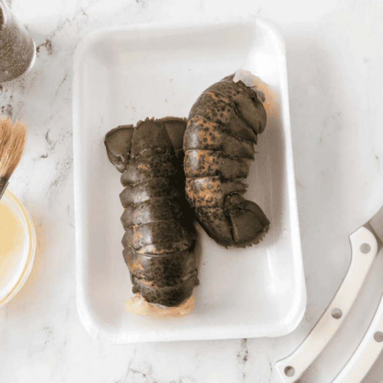 Frozen lobster tails, melted butter, salt, pepper and kitchen shears laid out on a counter