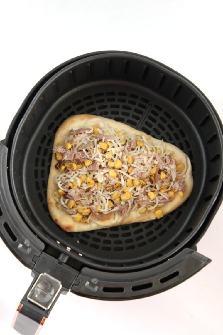 Two carnitas flatbreads cooking in an air fryer basket with melted cheese