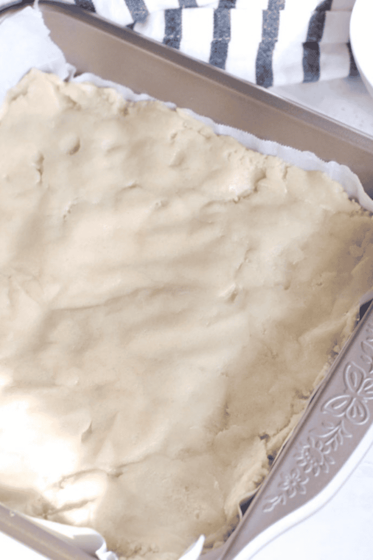 Sugar cookie dough spread evenly in an 8x8-inch parchment-lined pan, ready for the air fryer.