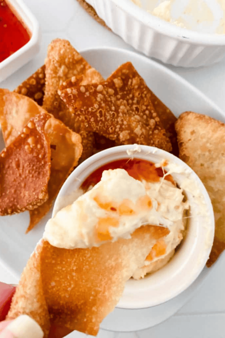Crispy golden air fryer wonton chips piled in a white bowl with a dish of dipping sauce