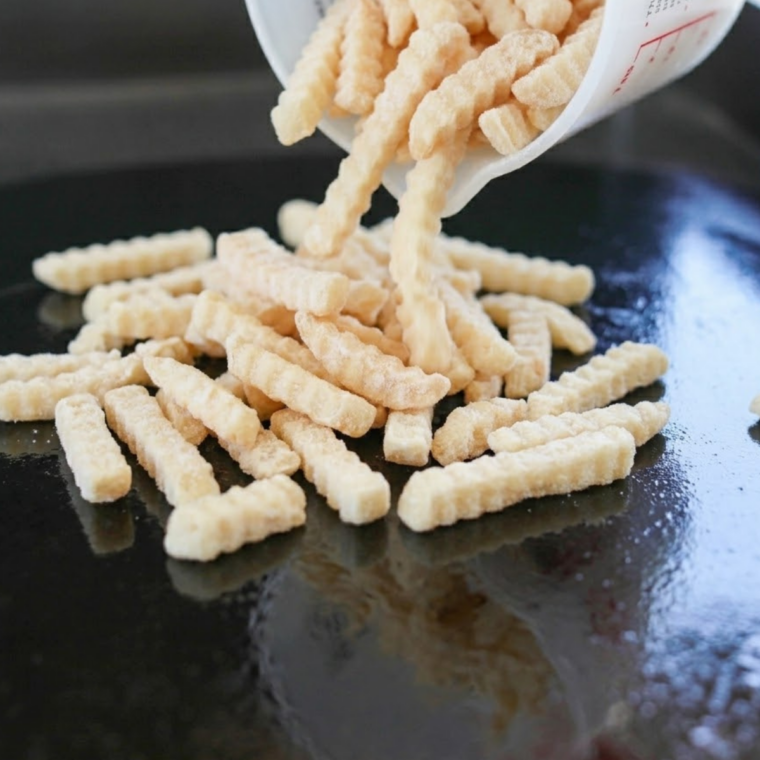 Seasoned frozen French fries crisping up on a Blackstone griddle surface.