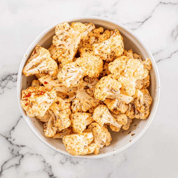 Frozen cauliflower florets in a bowl being coated with olive oil and seasonings before air frying.