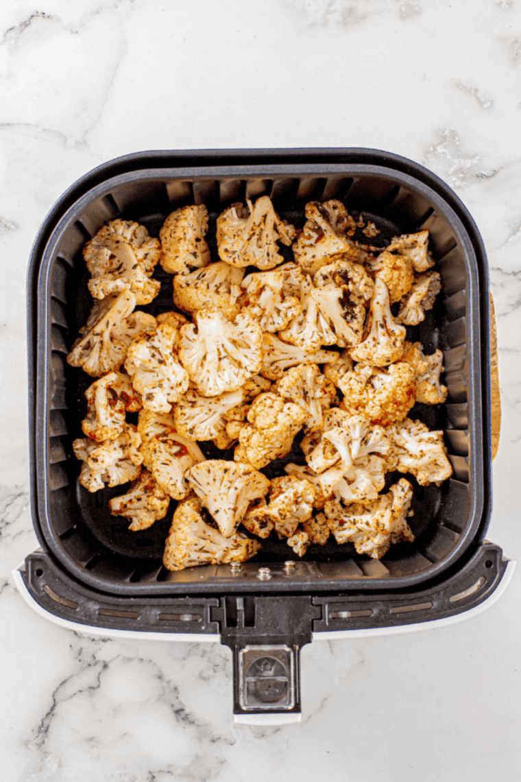 Seasoned cauliflower florets arranged in an air fryer basket, golden and crispy after cooking.