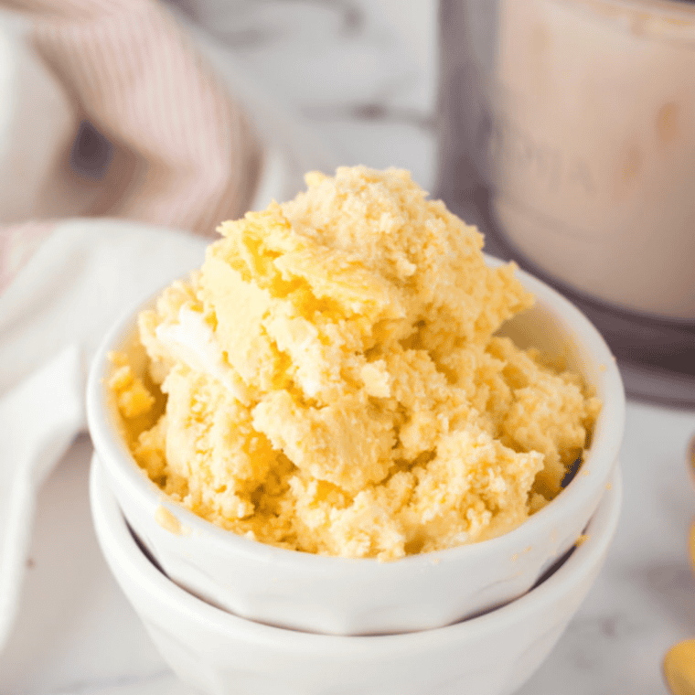 Creamy peach ice cream scooped from Ninja Creami pint into a bowl, garnished with fresh fruit.