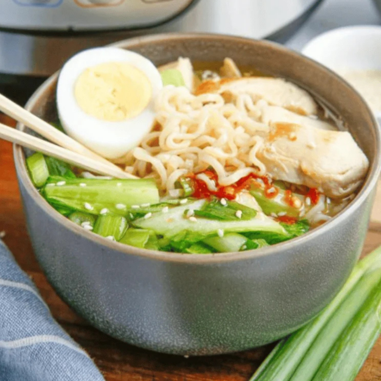 bowl of slow cooker chicken ramen topped with shredded chicken, a halved jammy egg and scallions