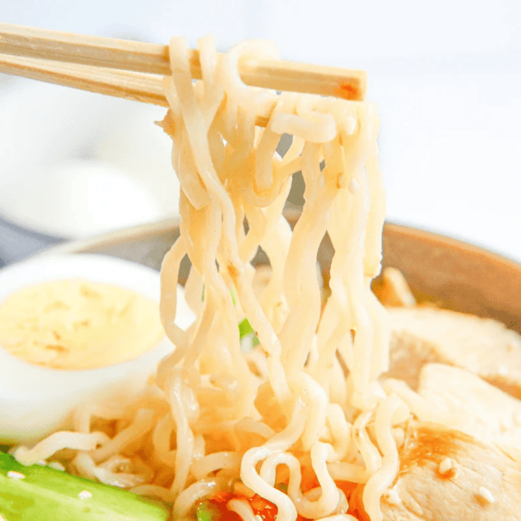 chopsticks pulling steaming noodles from a bowl of chicken ramen broth