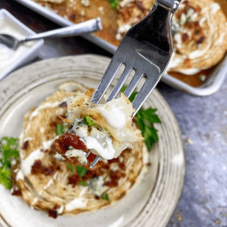 Air fryer loaded cabbage steaks topped with melted cheese and crispy bacon on a serving plate.