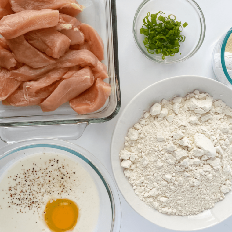 Chicken tenders prepared for breading station with dry coating setup and flattened chicken breasts for even cooking