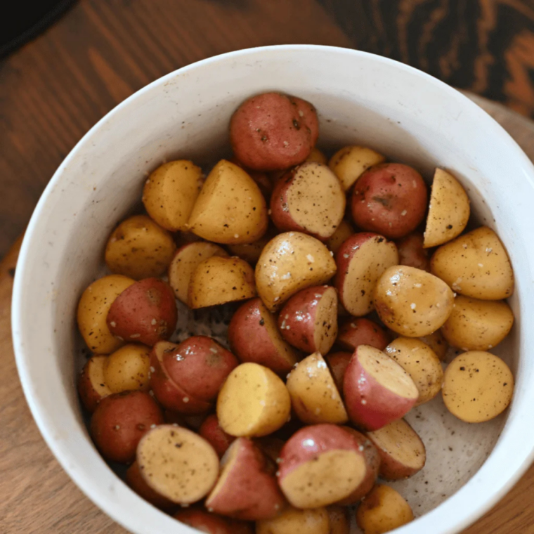 Potatoes tossed in a bowl with oil, salt, pepper, garlic powder, and paprika until evenly coated for seasoning before cooking on a griddle