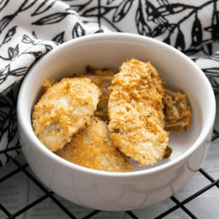 Crispy air fryer artichoke hearts stacked on a white plate with a bowl of dipping sauce