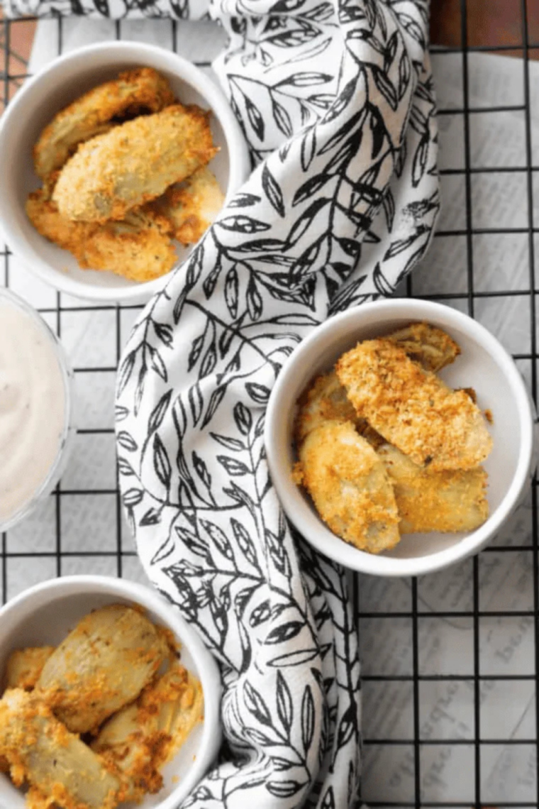 Hand dipping a crispy air fryer artichoke heart into creamy sauce