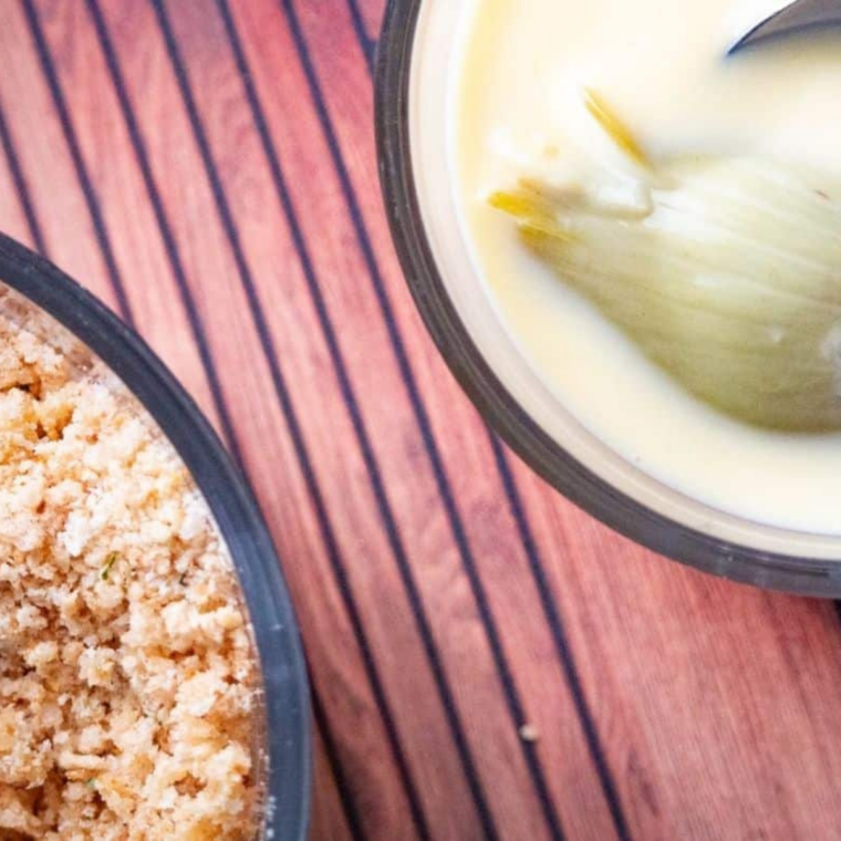 Artichoke hearts being dipped in egg wash and rolled in seasoned breadcrumbs