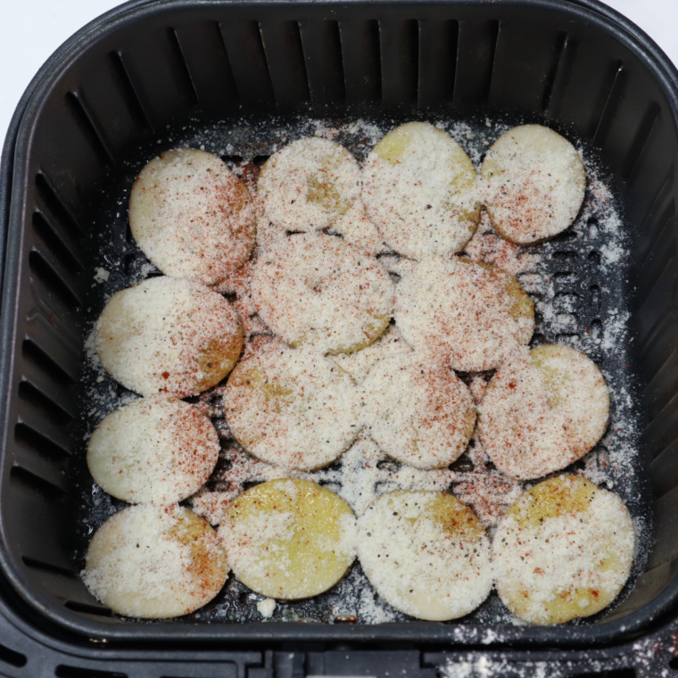 Potato slices being tossed in a mixing bowl with olive oil and seasonings like garlic powder, paprika, and oregano for even coating before air frying.