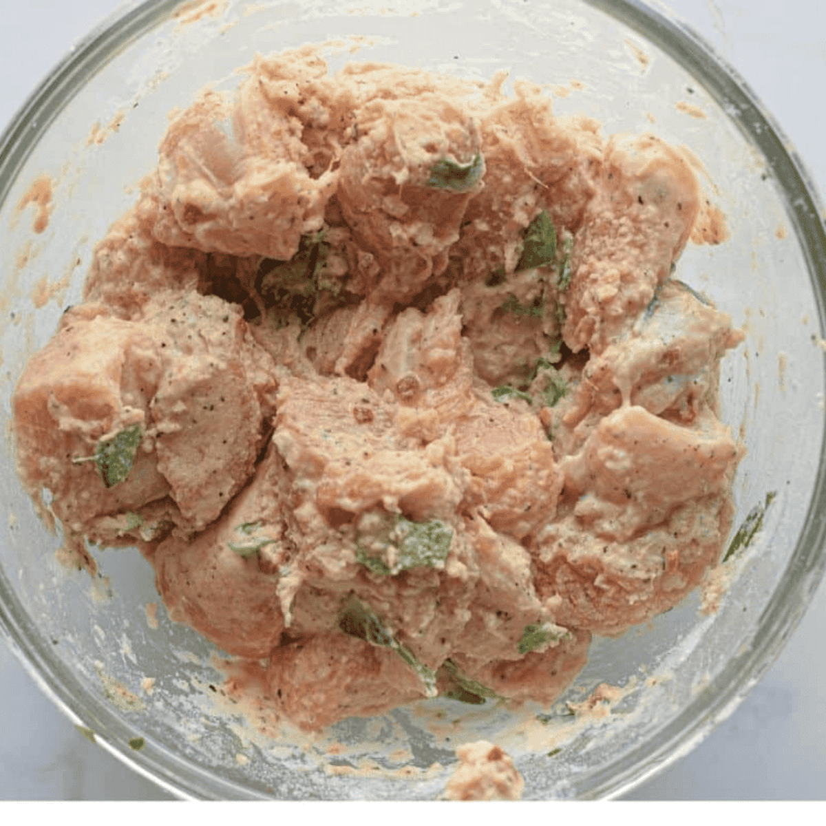 Mixing diced chicken with cornstarch, rice flour, spices, yogurt, curry leaves, egg white, and red food coloring for an even coating.