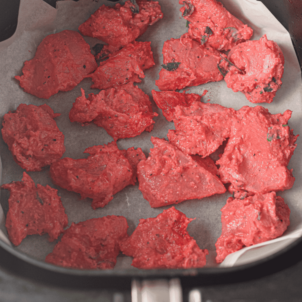 Marinated chicken pieces arranged in a single layer in the air fryer basket for even cooking.