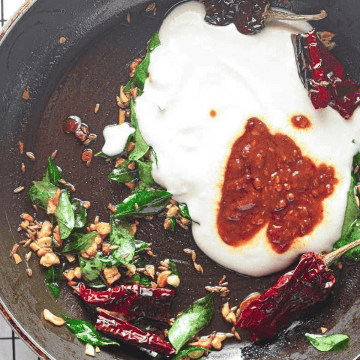 Preparing Chicken 65 sauce by sautéing cumin, curry leaves, and garlic, then adding yogurt, chili paste, cornstarch, sugar, salt, and pepper until slightly thickened.