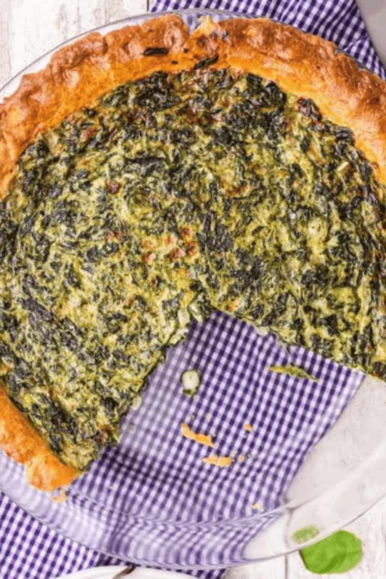 Slice of spinach quiche showing creamy egg filling with spinach and melted cheese in a golden flaky crust.