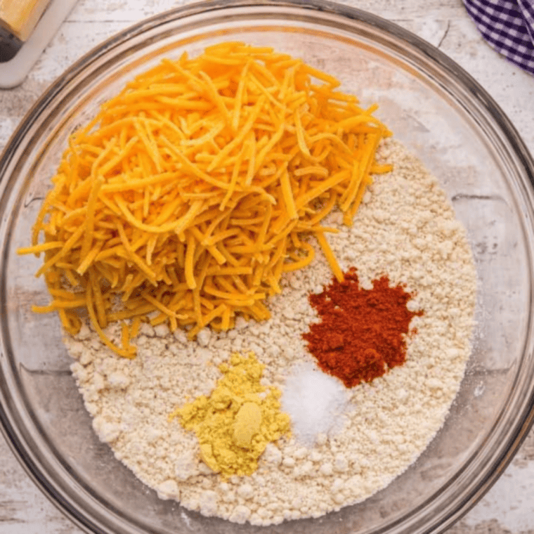 Hands mixing flour and butter with spices and cheese to form dough for spinach quiche crust on a clean countertop.