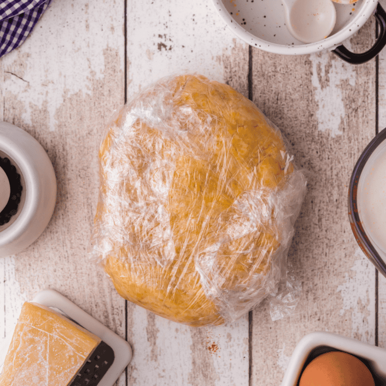 Quiche dough wrapped in plastic cling film resting in the refrigerator to chill before baking.