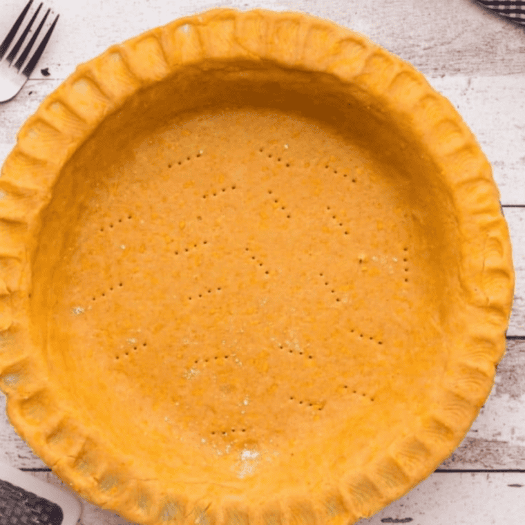 Rolled pastry lining a pie dish with fork-crimped edges and pricked base, being baked until golden brown in air fryer or oven.