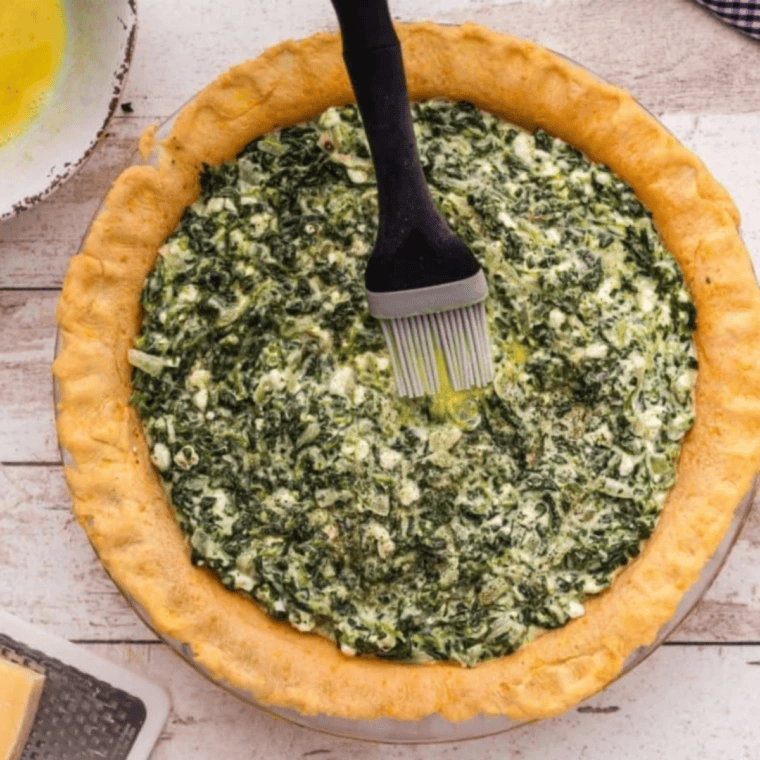 Quiche filled pastry crust brushed with egg wash, baking until golden and set in air fryer or oven with creamy spinach filling inside.