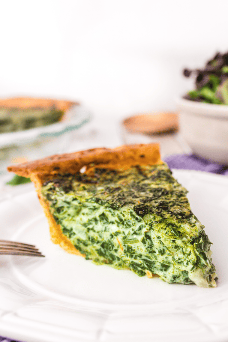Slice of spinach quiche showing creamy egg filling with spinach and melted cheese inside a golden flaky crust.