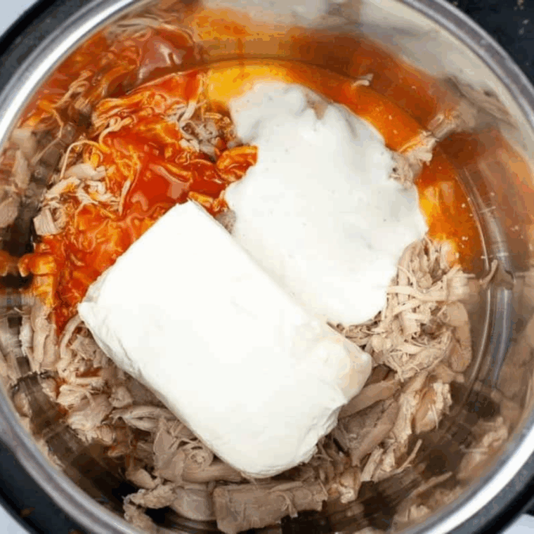 Instant Pot with cream cheese, Buffalo sauce, ranch dressing, and shredded cheese being stirred into a creamy dip