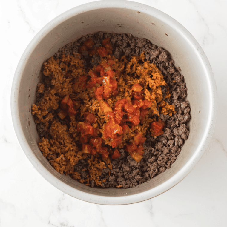 Ground beef browning in a large skillet, broken apart with a wooden spoon