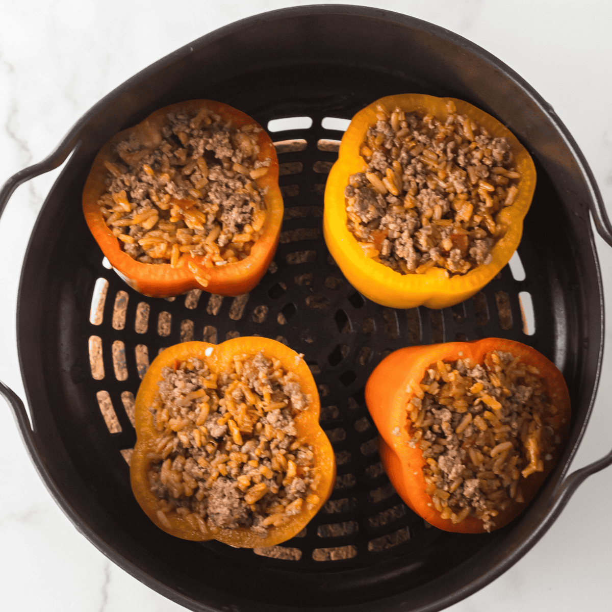 Bell peppers filled with picadillo standing upright in an air fryer basket
