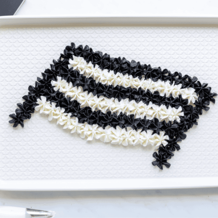 Two piping bags filled with white and black buttercream, fitted with 1M tips, ready to pipe onto a food-safe baking sheet or charcuterie board.