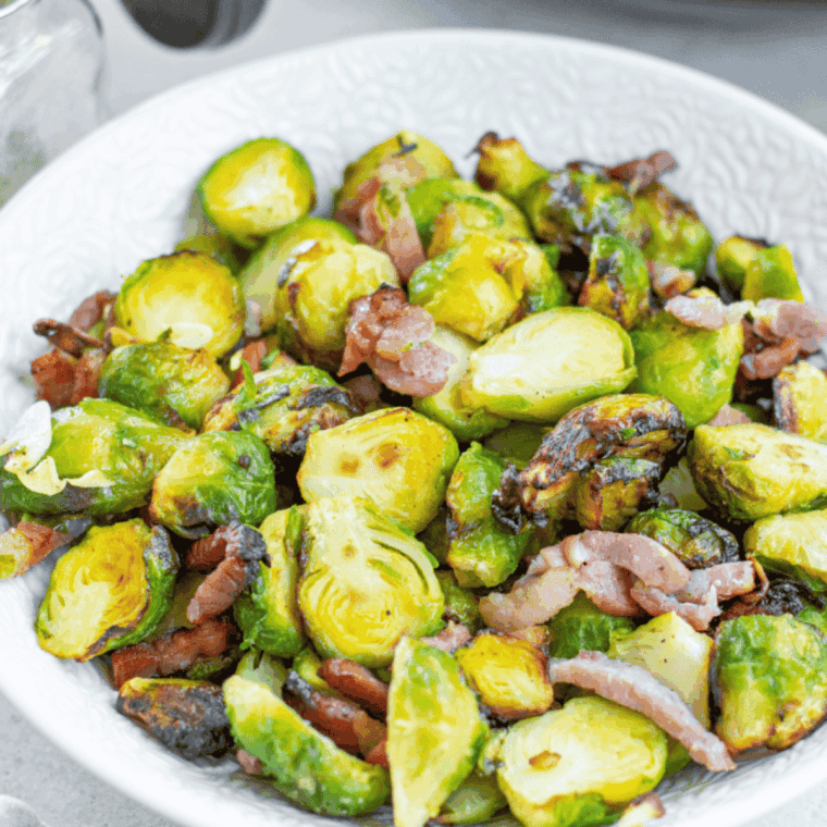 Crispy, golden-brown Brussels sprouts tossed with bacon, olive oil, and seasonings in an air fryer-ready bowl.