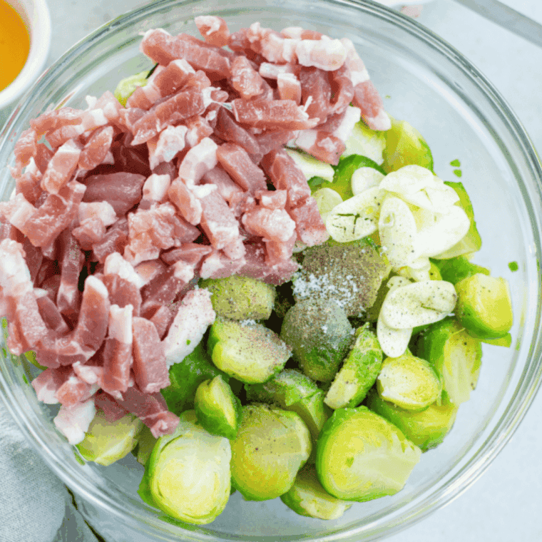 Brussels sprouts and chopped bacon tossed with olive oil, maple syrup, and seasonings in a large mixing bowl.