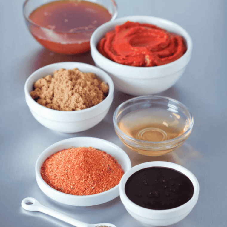 All ingredients for copycat McDonald's sweet and sour sauce arranged on a counter: apricot and peach preserves, corn syrup, vinegar, soy sauce, mustard, garlic powder, cornstarch, salt, cayenne, and food coloring.