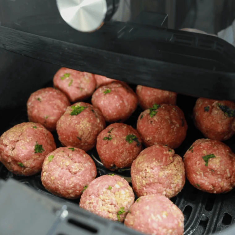 Raw meatballs arranged in a single layer with space in an air fryer basket