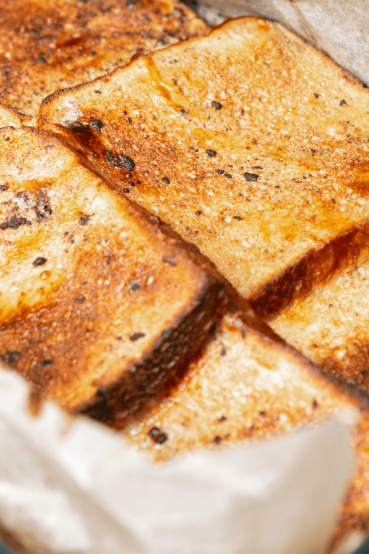 Air fryer eggless French toast slices, golden brown and crispy, served with maple syrup and fresh fruit on a plate