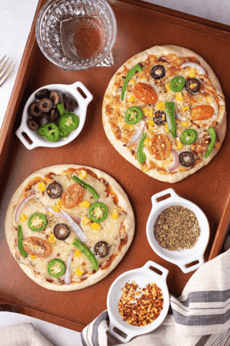 A whole wheat pita bread pizza with veggie toppings cooking inside a square air fryer basket.