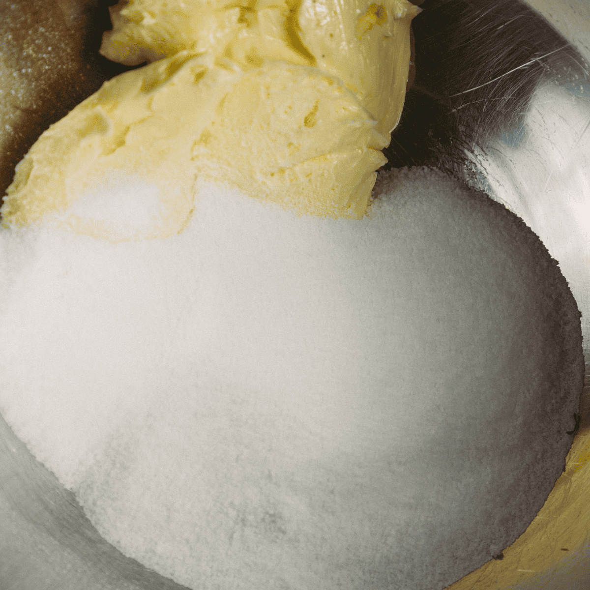 Mixing softened butter and sugar in a stand mixer until pale yellow for muffin batter.