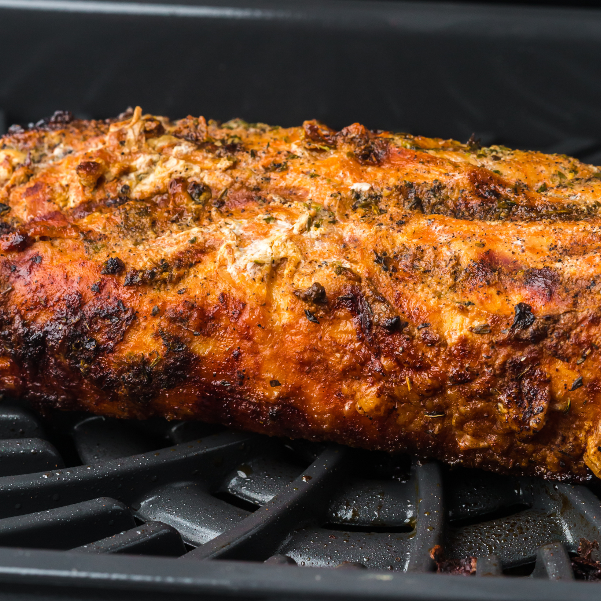 Cooked pork tenderloin resting on cutting board before slicing.