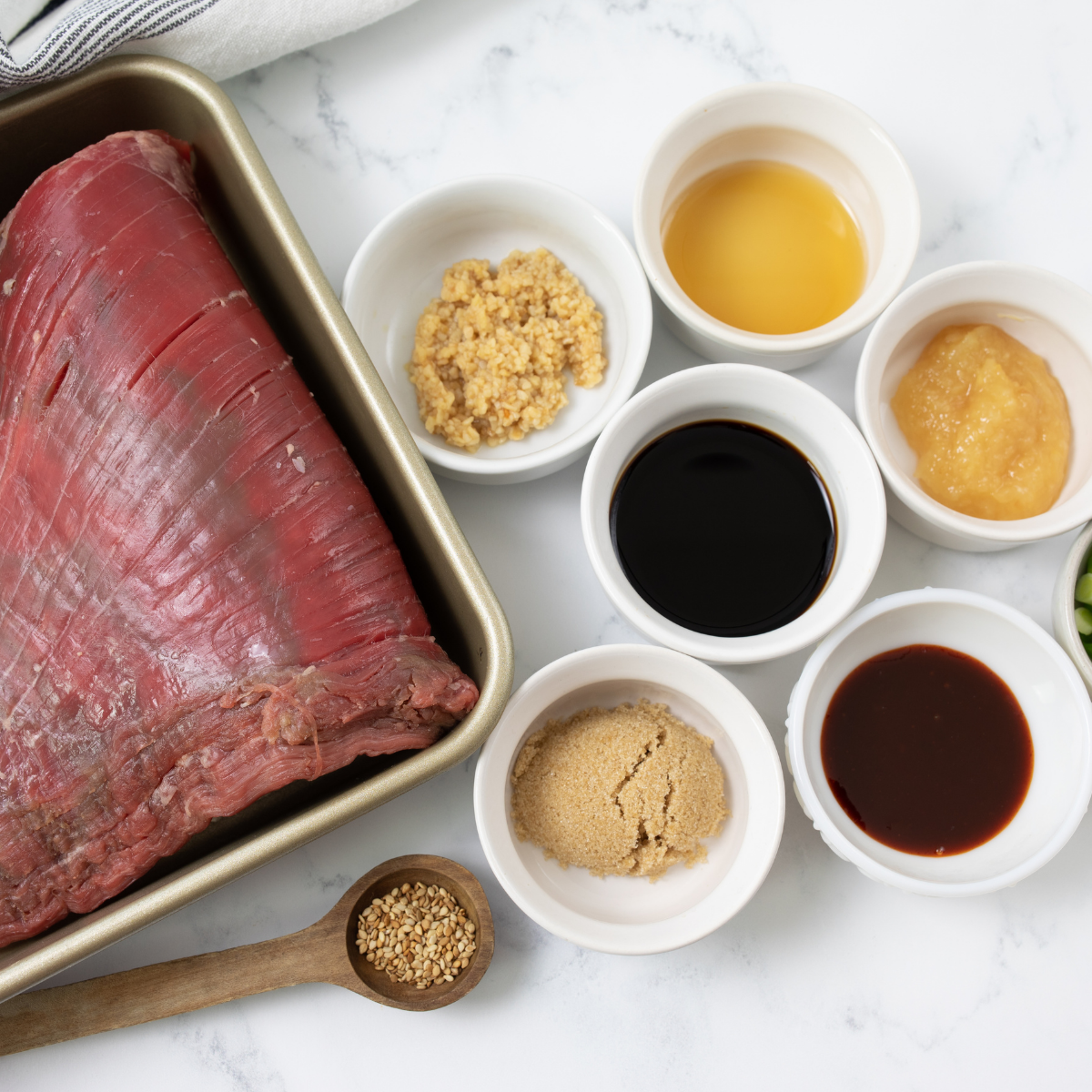 Flank steak with marinade ingredients including soy sauce, garlic, lime juice, and spices on a kitchen counter